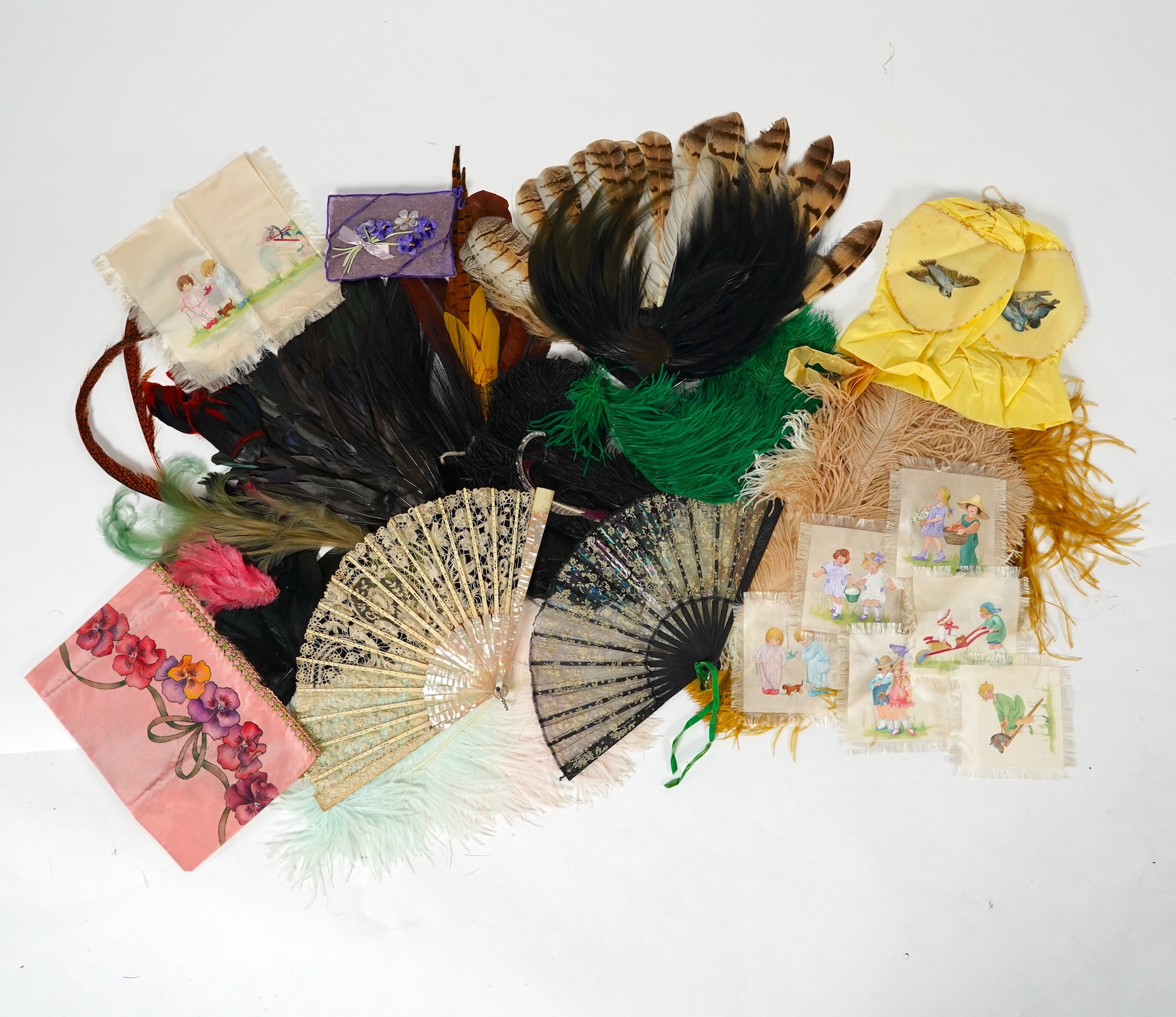 A collection of Edwardian exotic feather hat ornaments, with a collection of coloured ostrich feathers, two similar feather fans, a lace and another fan and silk hand painted mats